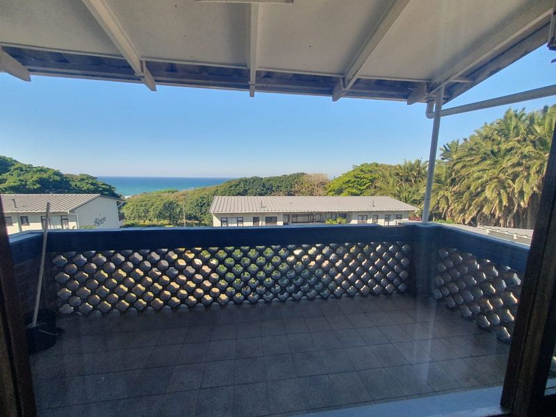 A covered balcony featuring tiled flooring and a decorative breeze block balustrade, offering pleasant views of the surrounding greenery and distant ocean.