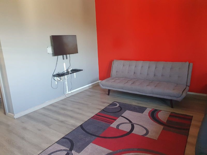 A living room featuring laminate flooring and a bold red accent wall, currently equipped with a wall-mounted television setup.