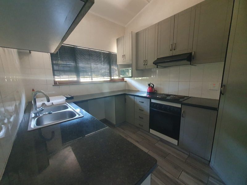 A functional kitchen featuring grey cabinetry, stone countertops, a double basin sink, and integrated appliances including an oven, hob, and extractor fan.