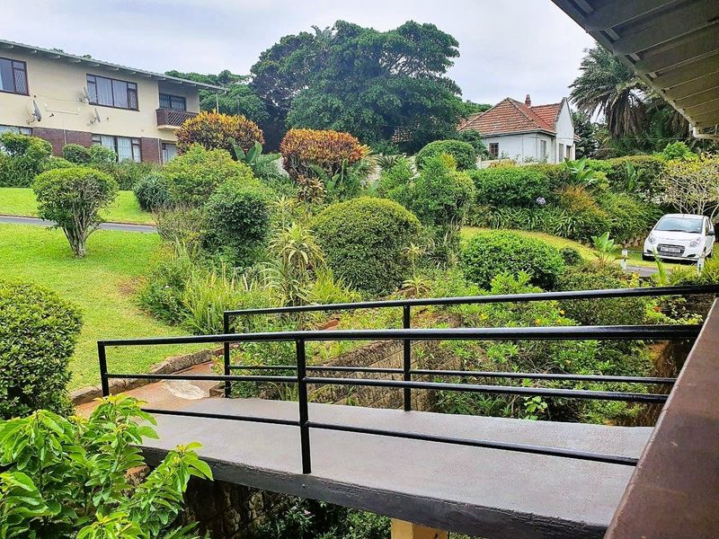 View of a well-maintained communal garden area featuring a metal pedestrian bridge and lush landscaping, viewed from an elevated position.