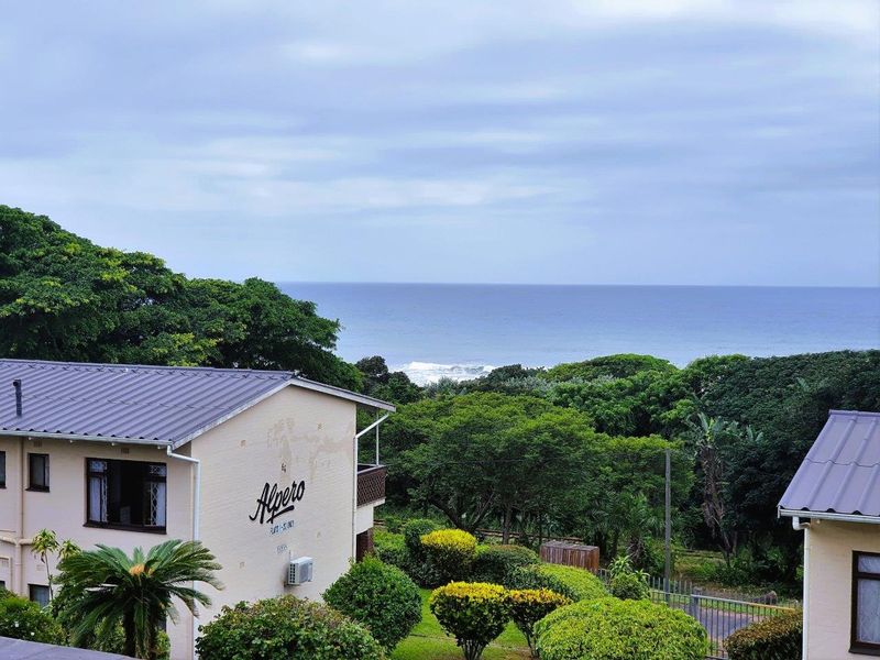 A scenic elevated view overlooking the ocean, featuring lush greenery, landscaped gardens, and the exterior facade of the apartment building.