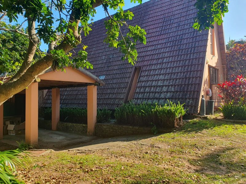 Rear view of the property featuring a steep tiled roof, a covered carport area, and established garden surroundings.