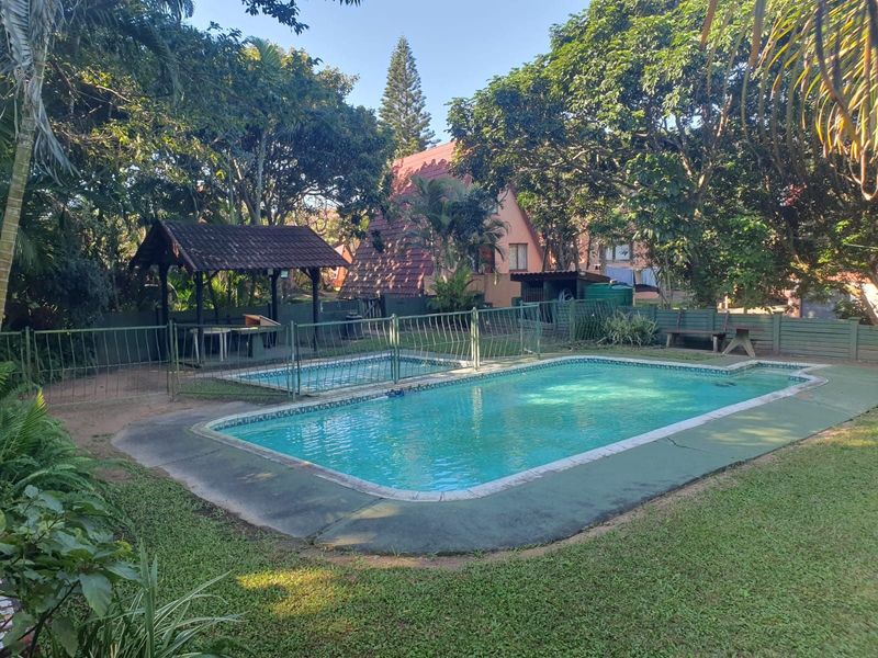 Outdoor pool area featuring a swimming pool with surrounding paving, lawn, and a covered gazebo structure in a garden setting.