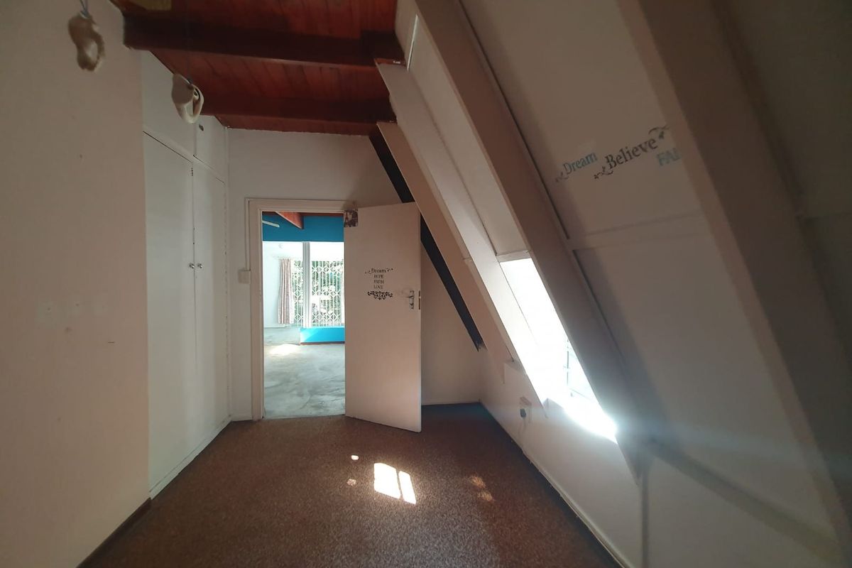 An attic-style bedroom featuring exposed timber ceiling beams, built-in cupboards, and a sloped ceiling, offering a unique architectural space ready for modernization.