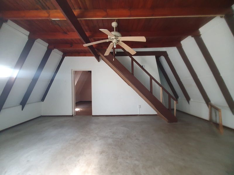 Spacious attic-style living area featuring exposed timber beams, a central staircase, and concrete flooring, offering a versatile blank canvas for renovation.
