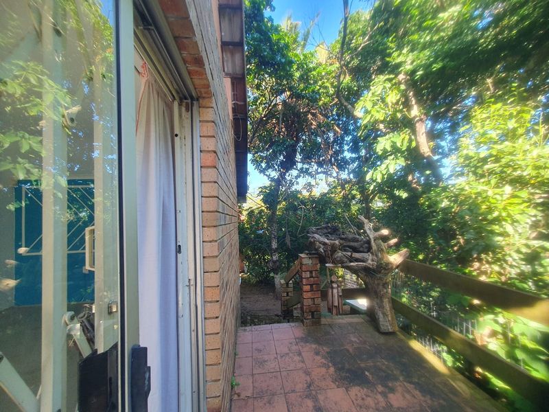 A weathered outdoor patio area featuring brick walling, tiled flooring, and a timber railing, overlooking a lush garden setting.