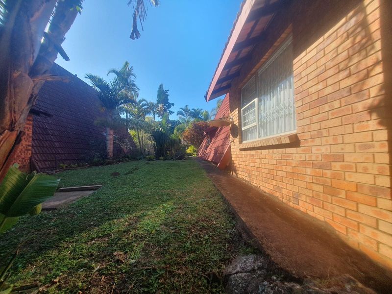 Rear exterior view of the apartment building featuring face brick walls, security window bars, and a private garden area with a concrete pathway.
