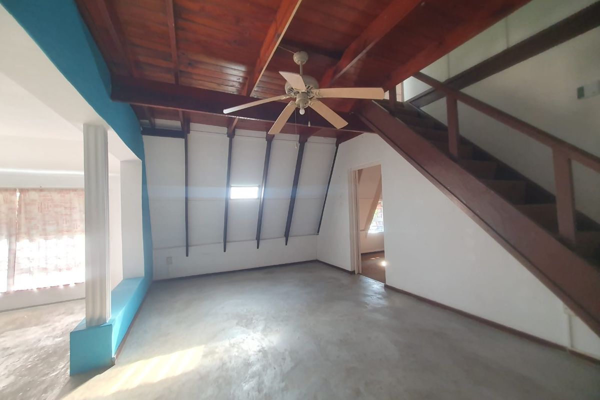 An open-plan living area featuring an exposed timber ceiling, a wooden staircase, and concrete flooring, offering a rustic architectural aesthetic.
