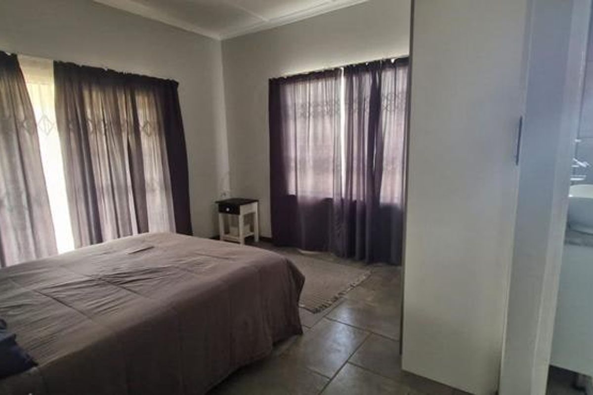 Bedroom featuring tiled flooring and an open-plan en-suite bathroom with a vessel sink and toilet, complemented by natural light through large windows.