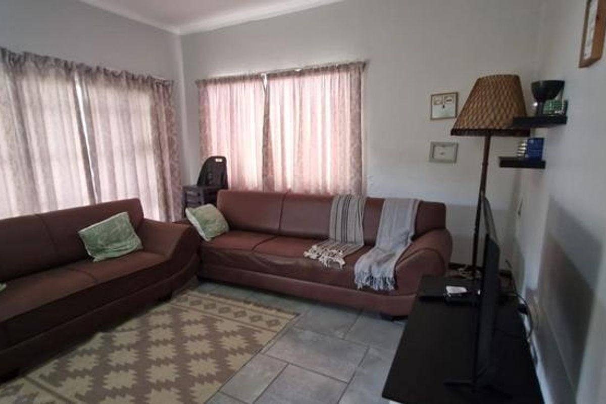 A comfortable living room featuring tiled flooring and large windows with curtains, providing a functional and well-lit space for relaxation.