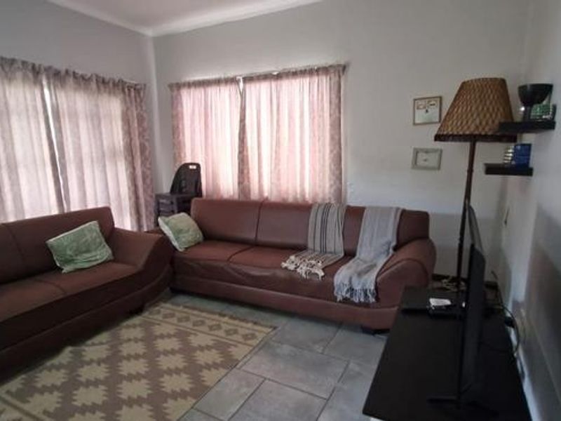 A comfortable living room featuring tiled flooring and large windows with curtains, providing a functional and well-lit space for relaxation.
