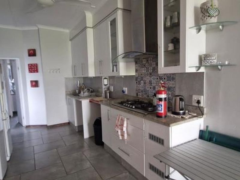 A functional kitchen featuring white cabinetry, stone countertops, a gas hob, built-in oven, and tiled flooring with a decorative backsplash.