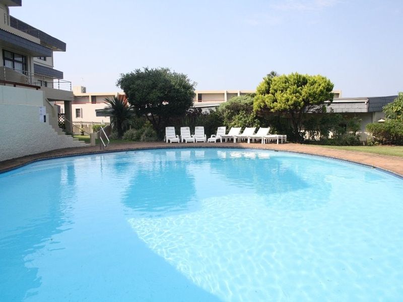 A communal swimming pool area featuring a circular pool with brick paving and surrounding landscaped garden space.