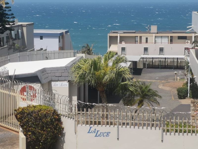 Elevated view overlooking the La Luce apartment complex grounds, featuring paved parking areas, perimeter security fencing, and a backdrop of the ocean.