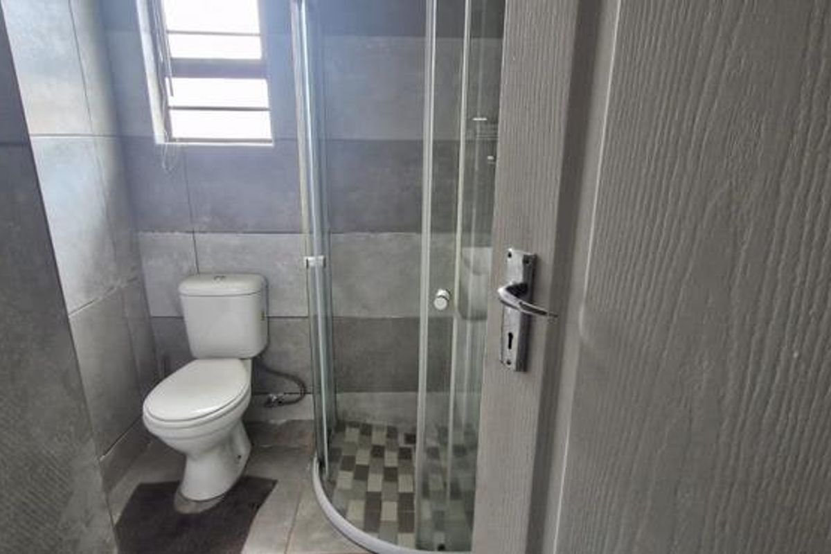 A compact bathroom featuring a corner shower enclosure, a standard toilet, and modern grey-toned wall and floor tiling.