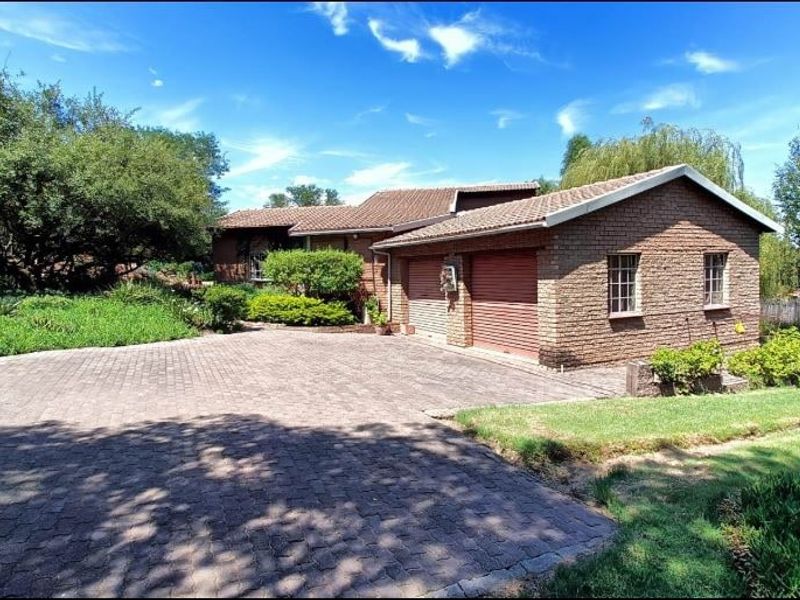 A well-maintained brick house featuring a double garage, a spacious paved driveway, and established garden surroundings.