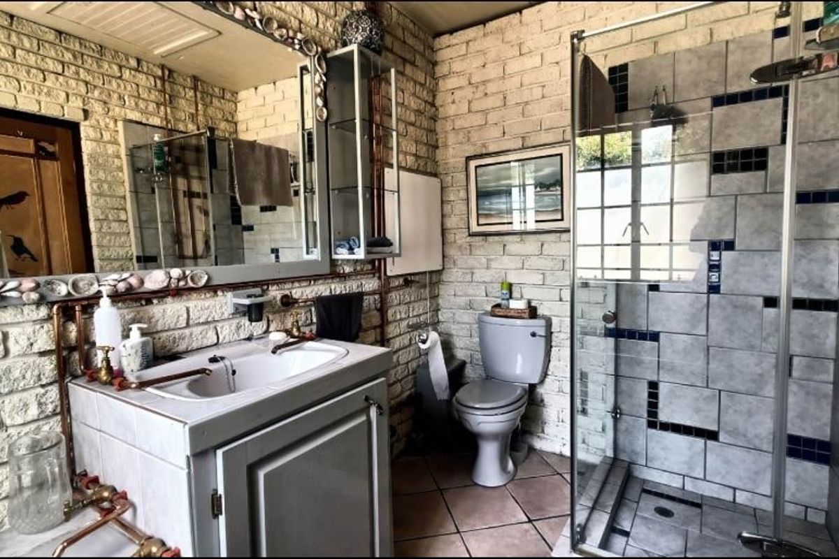 A bathroom featuring exposed brick walls, a vanity with a ceramic basin, a glass-enclosed shower, and tiled flooring with dated finishes.