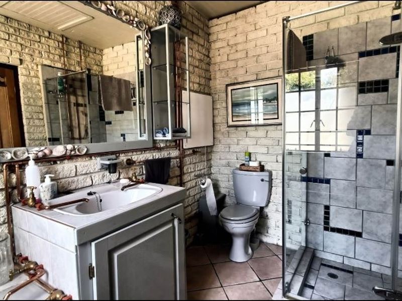 A bathroom featuring exposed brick walls, a vanity with a ceramic basin, a glass-enclosed shower, and tiled flooring with dated finishes.