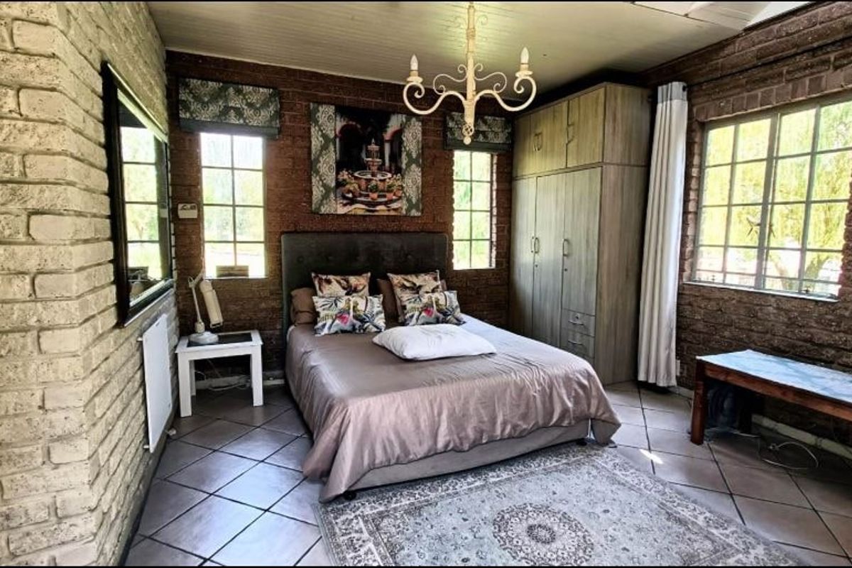 A rustic-style bedroom featuring exposed brick walls, tiled flooring, built-in cabinetry, and large windows providing natural light.