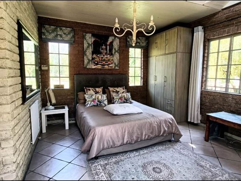 A rustic-style bedroom featuring exposed brick walls, tiled flooring, built-in cabinetry, and large windows providing natural light.