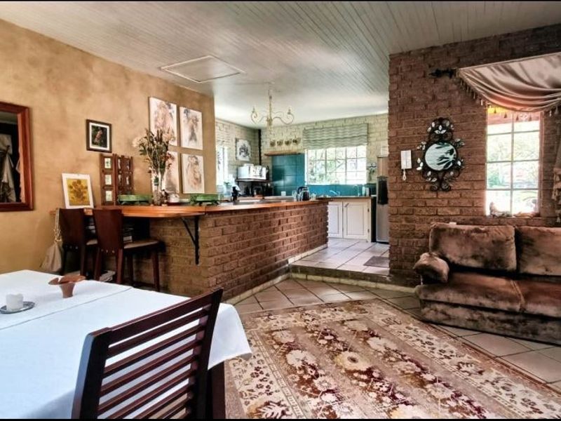 Open-plan living and dining area featuring exposed brickwork, a breakfast bar, and a functional kitchen with tiled flooring and timber ceiling details.