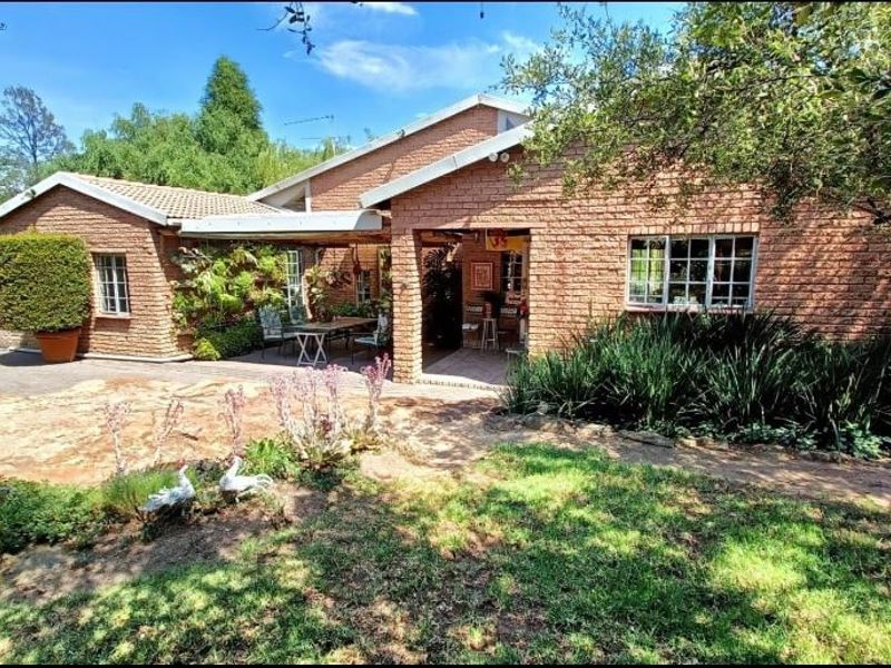 Rear view of a single-story brick house featuring a covered patio area, established garden, and paved outdoor space.