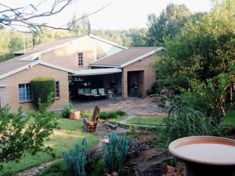 Rear view of a brick house featuring a covered patio area, retractable awning, and a well-established landscaped garden with stone pathways.