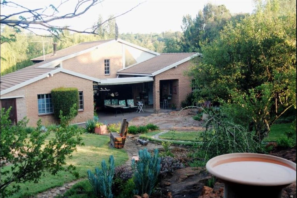 Rear view of a brick house featuring a covered patio area, retractable awning, and a well-established landscaped garden with stone pathways.