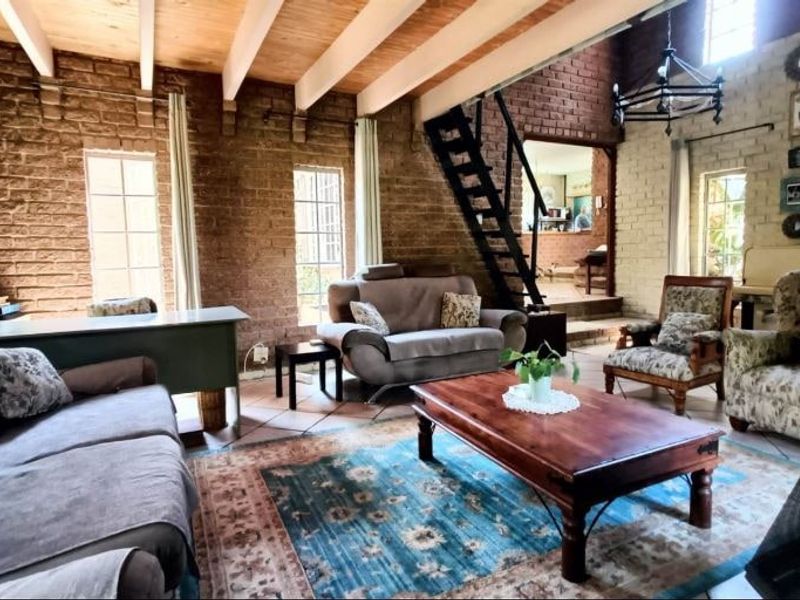 Spacious living room featuring rustic exposed brick walls, timber ceiling beams, and terracotta flooring, with a metal staircase leading to an upper level.