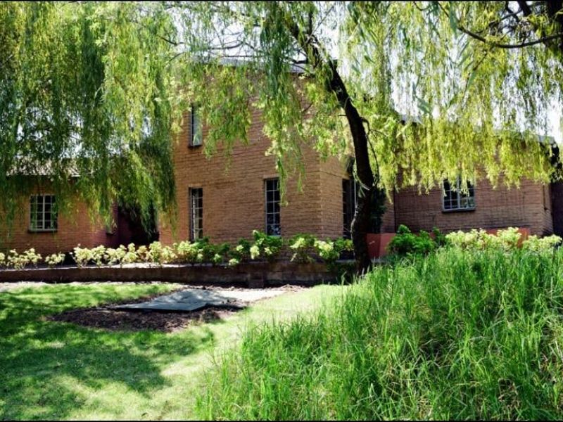 A view of the rear brick facade of the house, featuring established garden landscaping and mature trees.