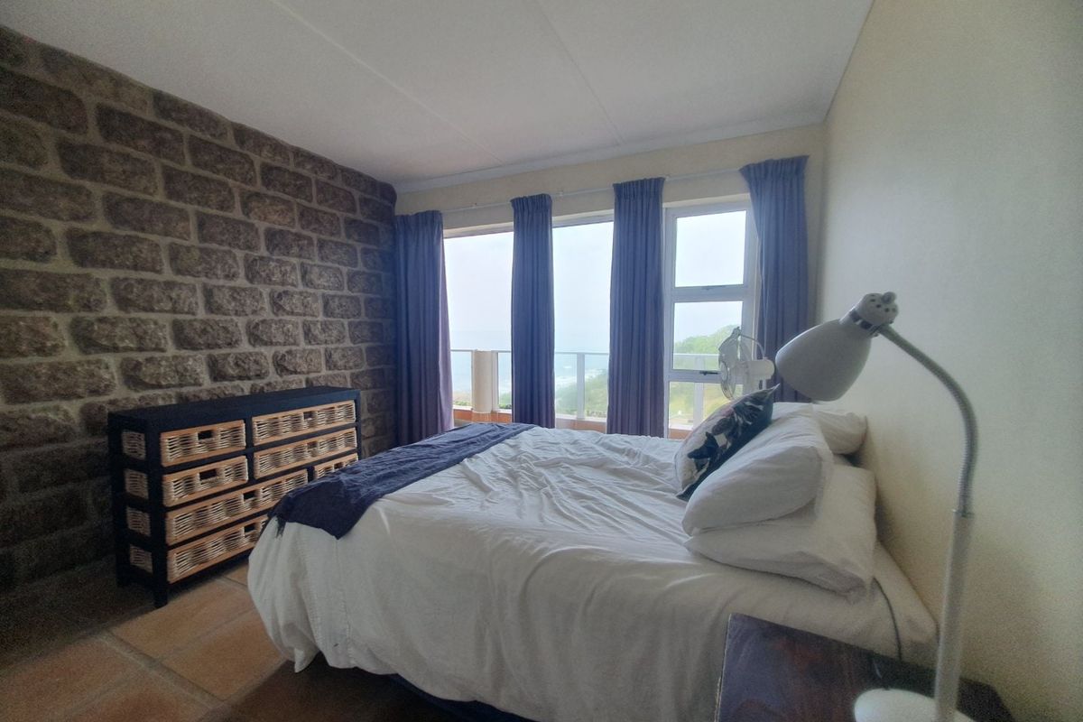A bedroom featuring a rustic stone accent wall, tiled flooring, and large windows providing natural light and access to a balcony.