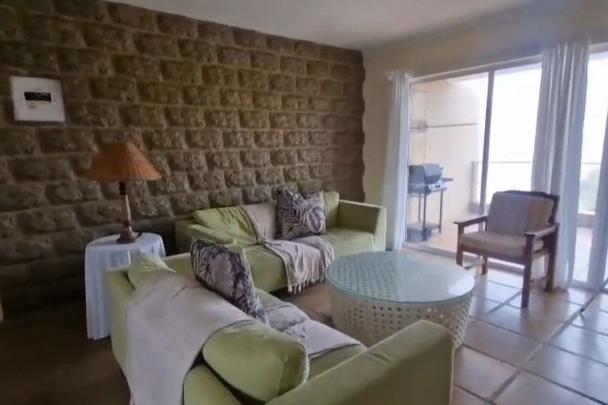 A living room featuring a prominent stone accent wall, tiled flooring, and large sliding glass doors providing access to an outdoor balcony area.