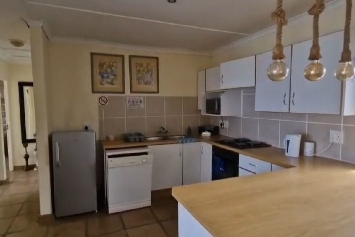 A functional kitchen featuring built-in cabinetry, laminate countertops, a gas hob, and a double basin sink with tiled backsplash and flooring.