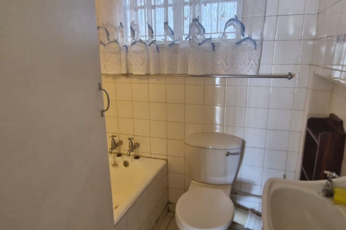 A compact bathroom featuring a standard bathtub, toilet, and pedestal basin with dated ceramic wall tiling and security bars on the window.