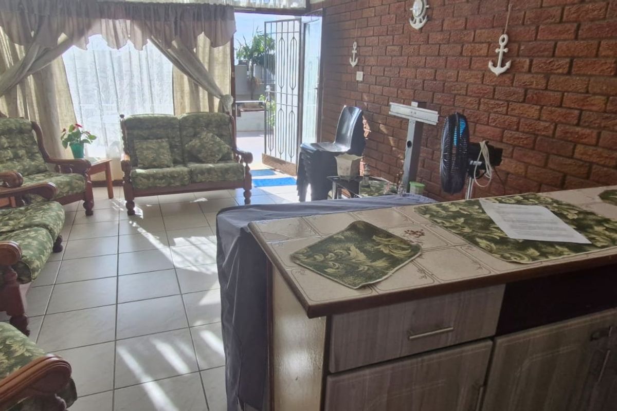 A living area featuring tiled flooring and an exposed brick feature wall, with direct access to an outdoor patio through a security gate.
