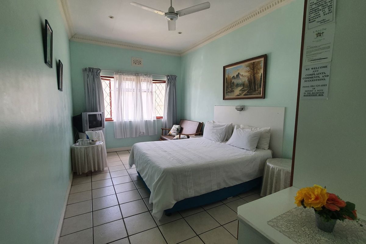 A functional bedroom featuring tiled flooring, a ceiling fan, and crown molding, providing a simple and comfortable sleeping space.