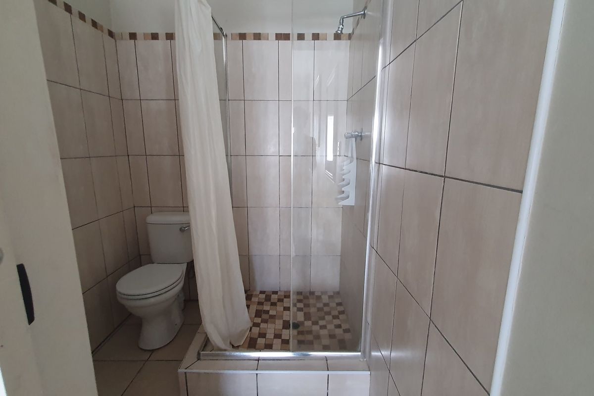 A functional bathroom featuring a tiled shower enclosure with a glass door and a standard toilet, finished with neutral wall and floor tiles.