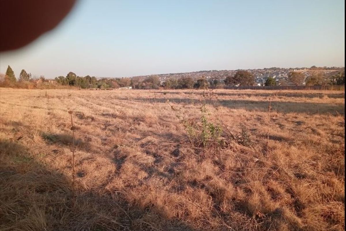 A wide-angle view of a vacant residential plot featuring dry grass and distant neighborhood views.