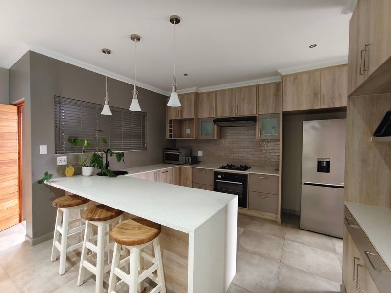 Modern kitchen featuring light wood cabinetry, stone countertops, a breakfast bar, integrated gas hob, oven, and extractor fan with neutral tiled flooring.