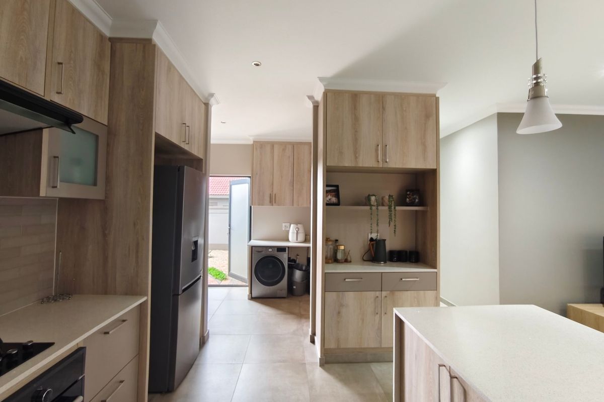 Modern kitchen featuring light wood-grain cabinetry, stone countertops, integrated appliances, and a seamless transition to a rear utility area with laundry connections.