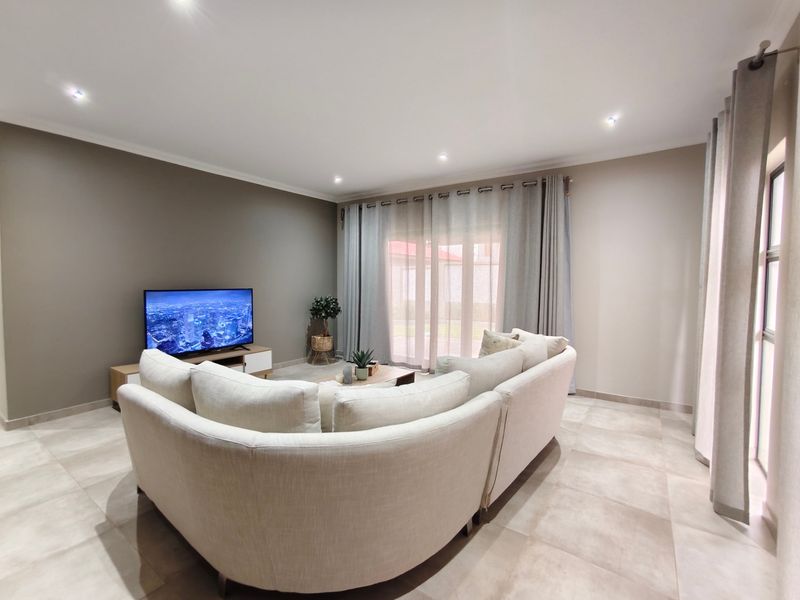 A well-maintained living room featuring neutral tiled flooring, recessed downlighting, and a large sliding glass door providing access to the outdoor area.