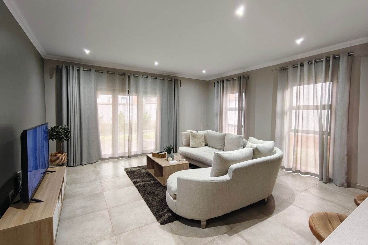 A bright and spacious living room featuring large sliding glass doors, neutral tiled flooring, and recessed downlighting, creating a comfortable and inviting atmosphere.