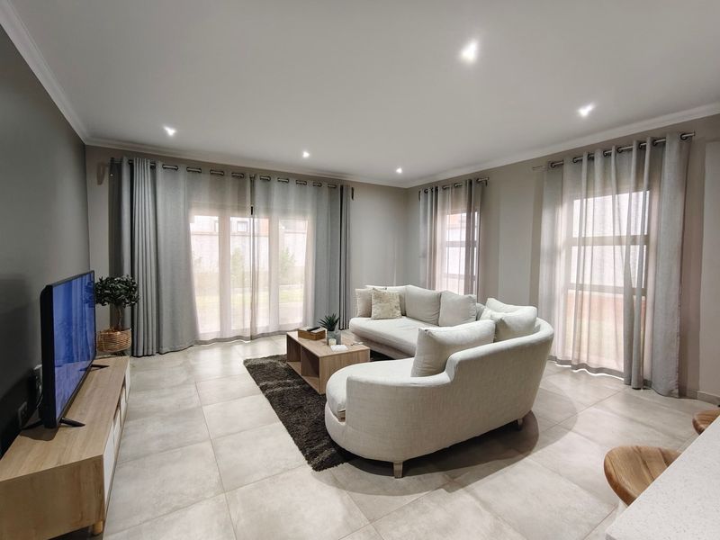 A bright and spacious living room featuring large sliding glass doors, neutral tiled flooring, and recessed downlighting, creating a comfortable and inviting atmosphere.