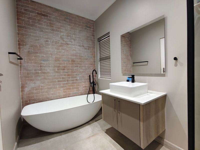 Modern bathroom featuring a freestanding bathtub, a wall-mounted vanity with a vessel sink, and a stylish exposed brick feature wall.
