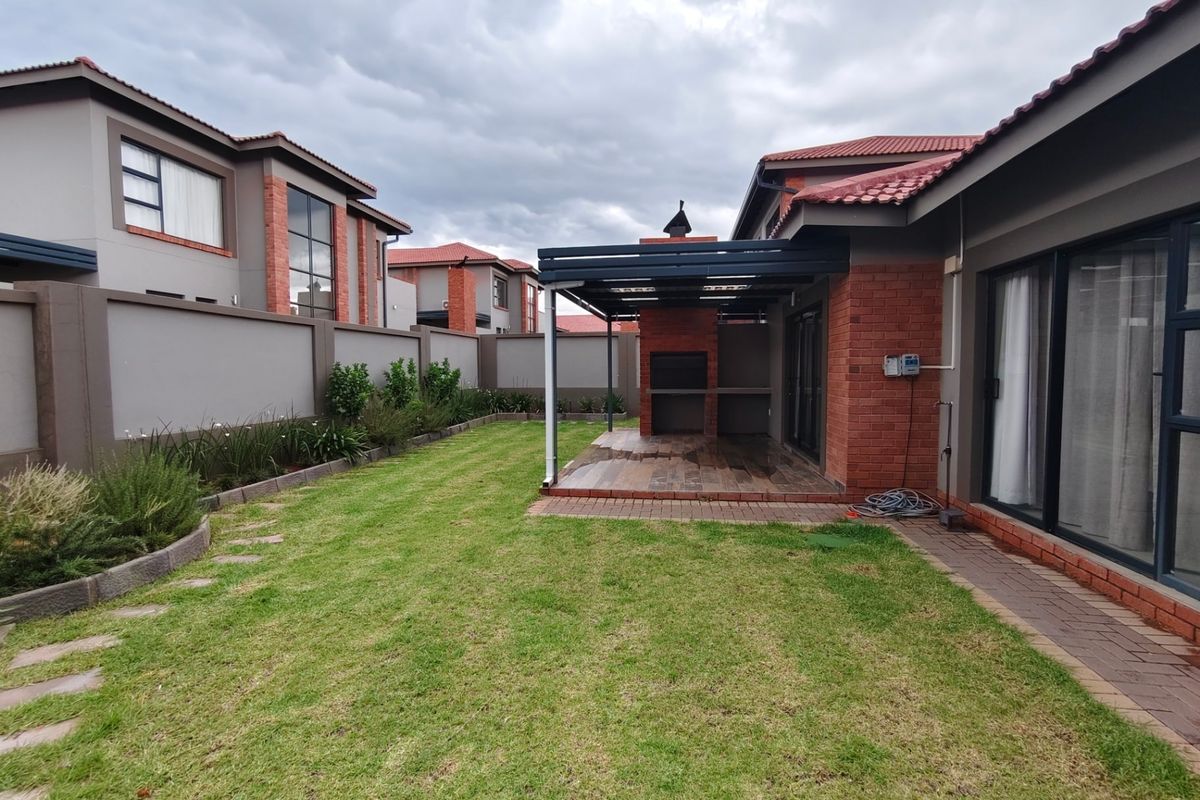 Rear garden featuring a covered patio with a built-in braai, brick perimeter walls, and a well-maintained lawn area.