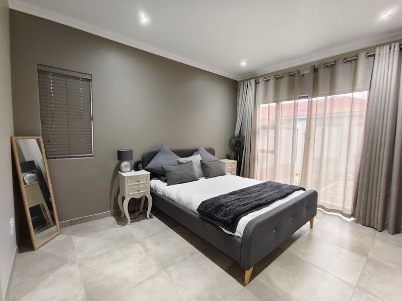 A well-maintained bedroom featuring neutral tiled flooring, recessed downlighting, and a large sliding glass door providing access to the exterior.