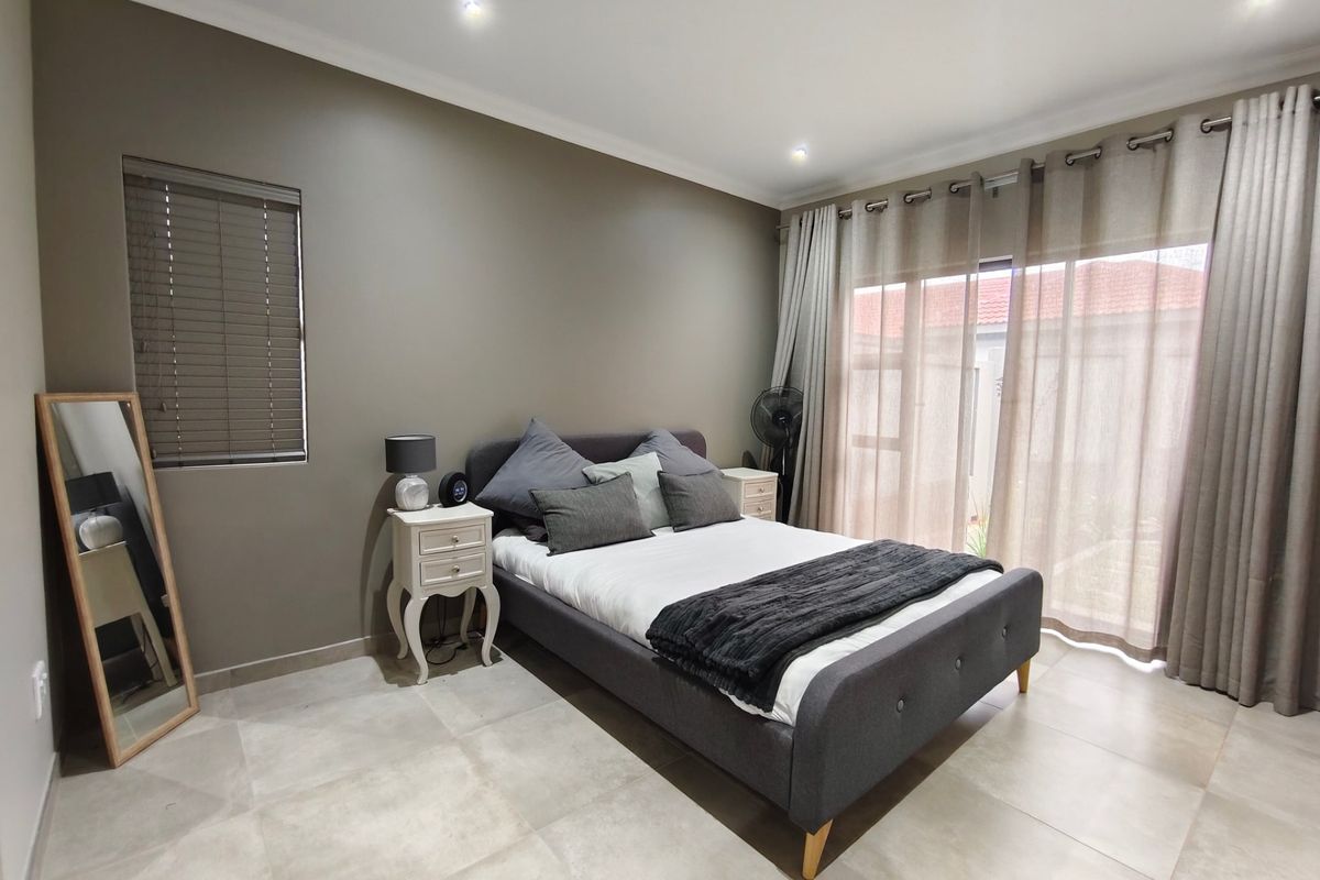 A well-maintained bedroom featuring neutral tiled flooring, recessed downlighting, and a large sliding glass door providing access to the exterior.