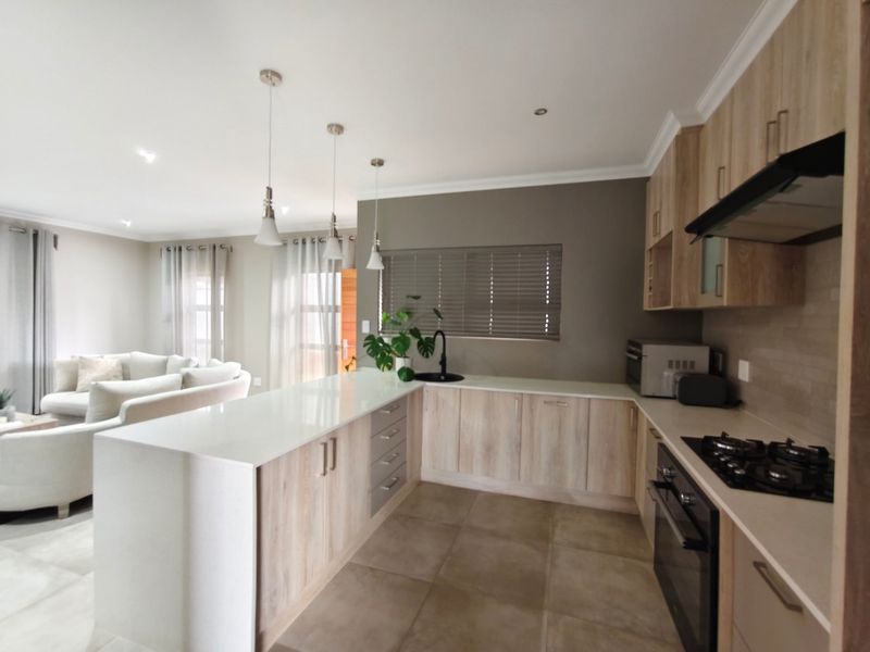 Modern open-plan kitchen featuring light wood cabinetry, quartz countertops, gas hob, and integrated appliances, seamlessly flowing into the adjacent living area.