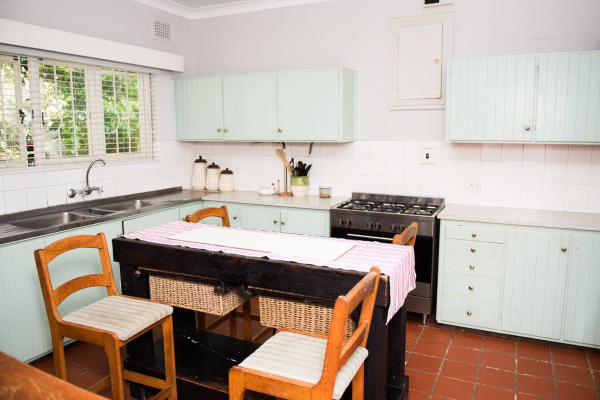 A functional kitchen featuring mint-colored cabinetry, a gas stove, stainless steel sink, and traditional terracotta floor tiles.