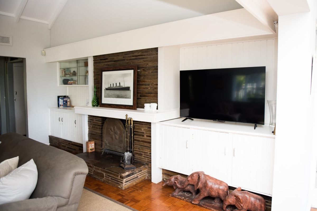 A cozy living room featuring a prominent stone fireplace, built-in white cabinetry, and classic parquet flooring under a vaulted ceiling.